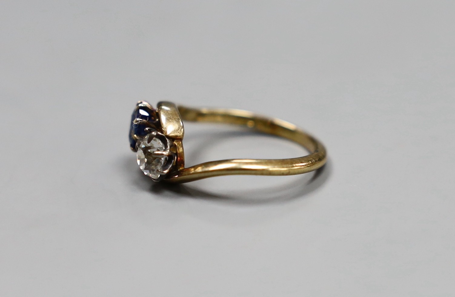 An early 20th century 18ct gold, sapphire and diamond two stone cross-over ring, size L, gross 3.2 grams